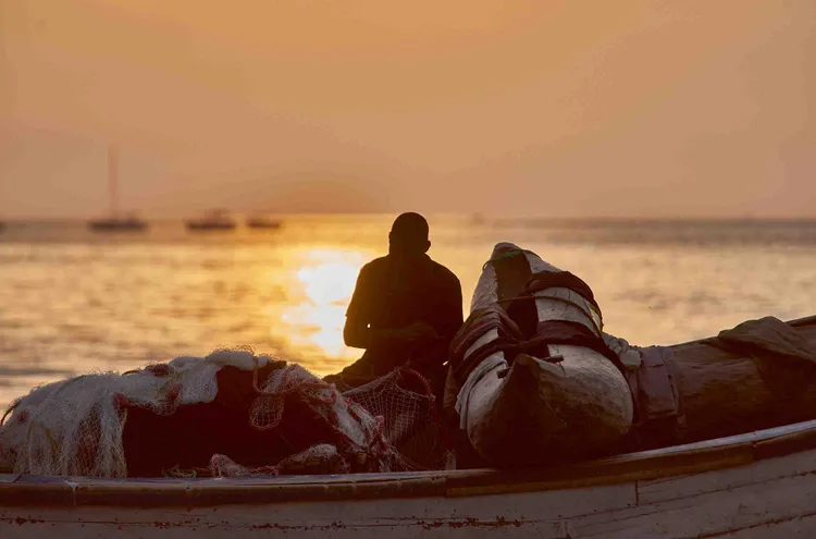 A fisherman mends his nets as the sun sets over the lake (image by Chosa Mweemba).