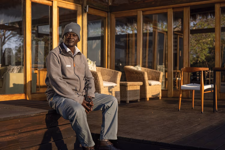 Isaac is tall with a broad nose pointed at its end and a short beard. Like Evidence, so too do his legs spread out in front of him to arrest what little warmth the fire gives. (Image by Chona Mweemba for Nkwazi Magazine).