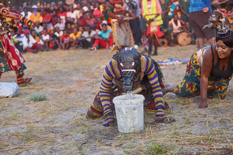 Likishi Ngulu (pig  spirit) exhibits a pig’s behaviour by playing in stagnant water and unkempt environments. His role is to entertain spectators. (Image by Nkwazi/Justine Kunda).